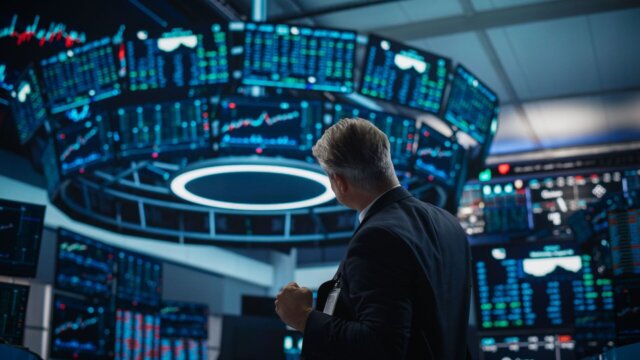 Stock trader observes market data on digital screens.